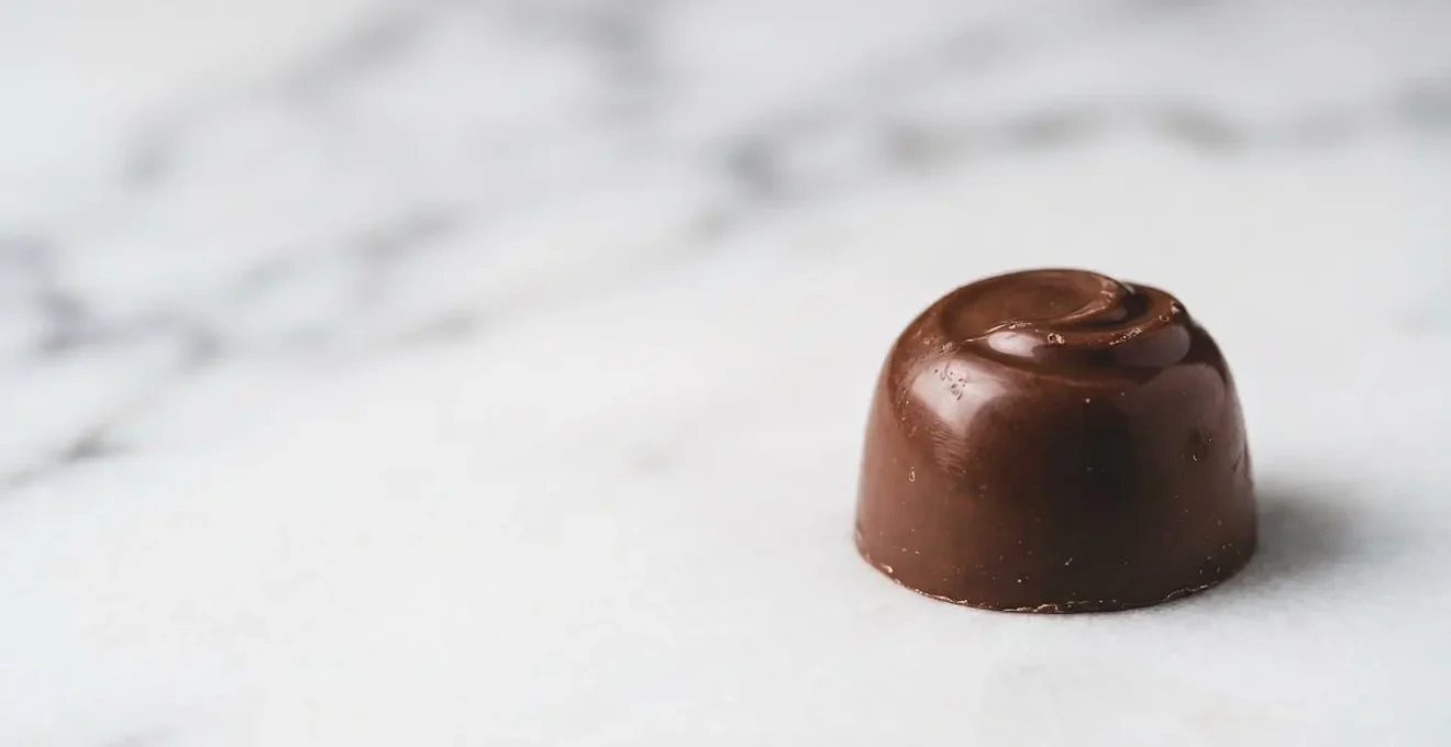Gros plan macro sur une praline belge artisanale posée sur une surface marbrée blanche avec beaucoup d'espace négatif
