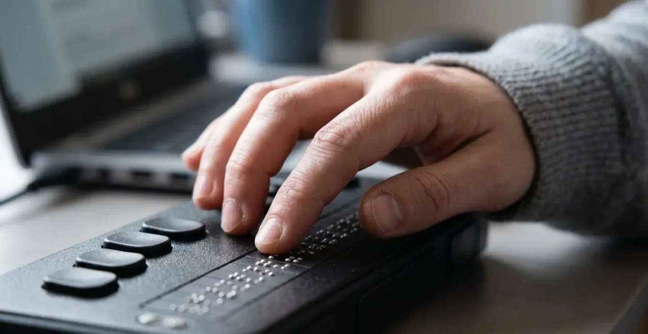 Gros plan sur les mains d'une personne utilisant un lecteur braille connecté à un ordinateur portable